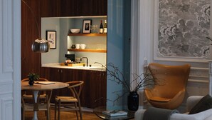 Een moderne keuken met houten kastjes, een eethoek met een ronde tafel en stoelen, en een gezellige zithoek met een bank en fauteuil.