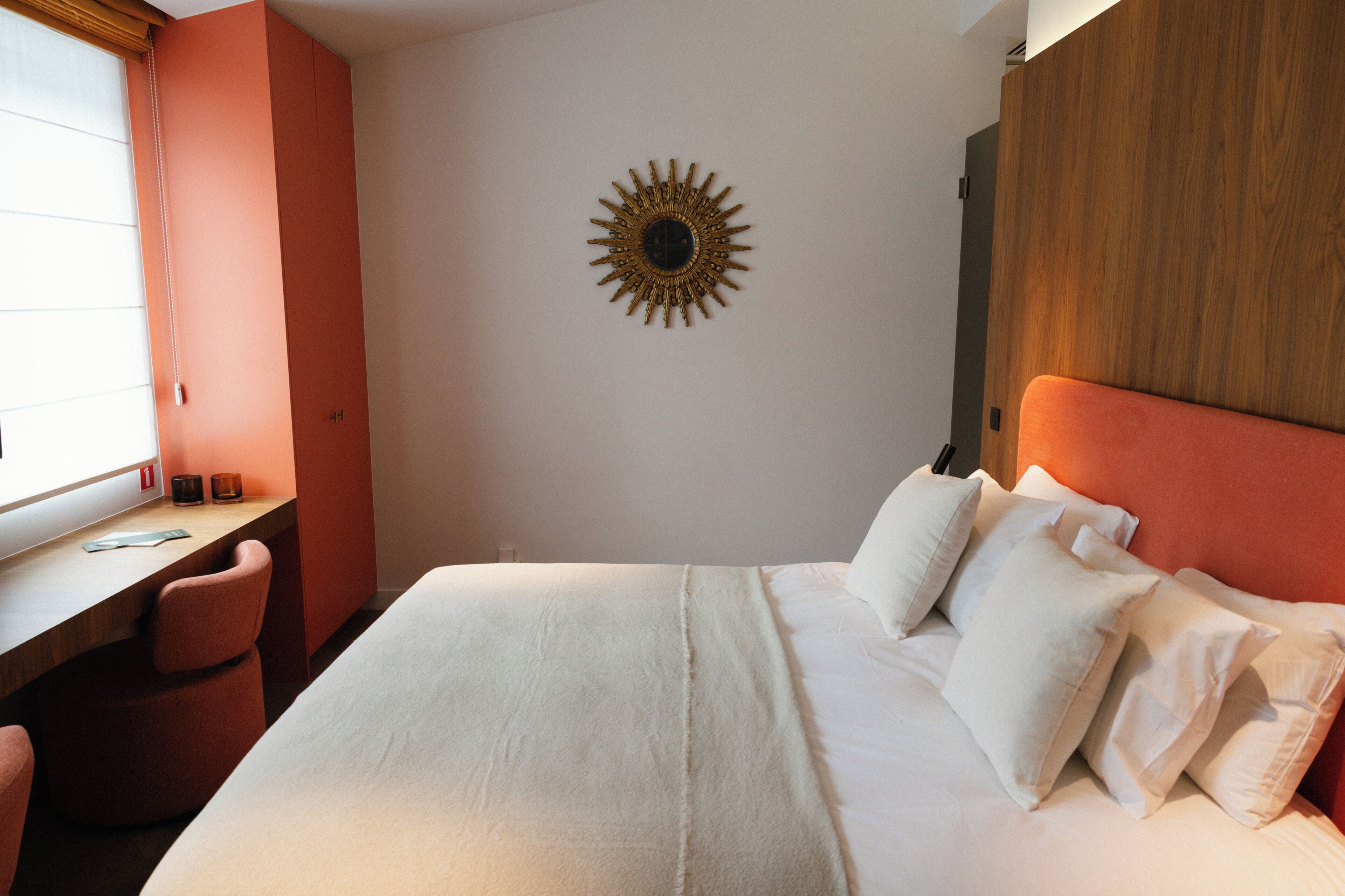 A hotel room with a bed, a desk, and a wall-mounted sun decoration.