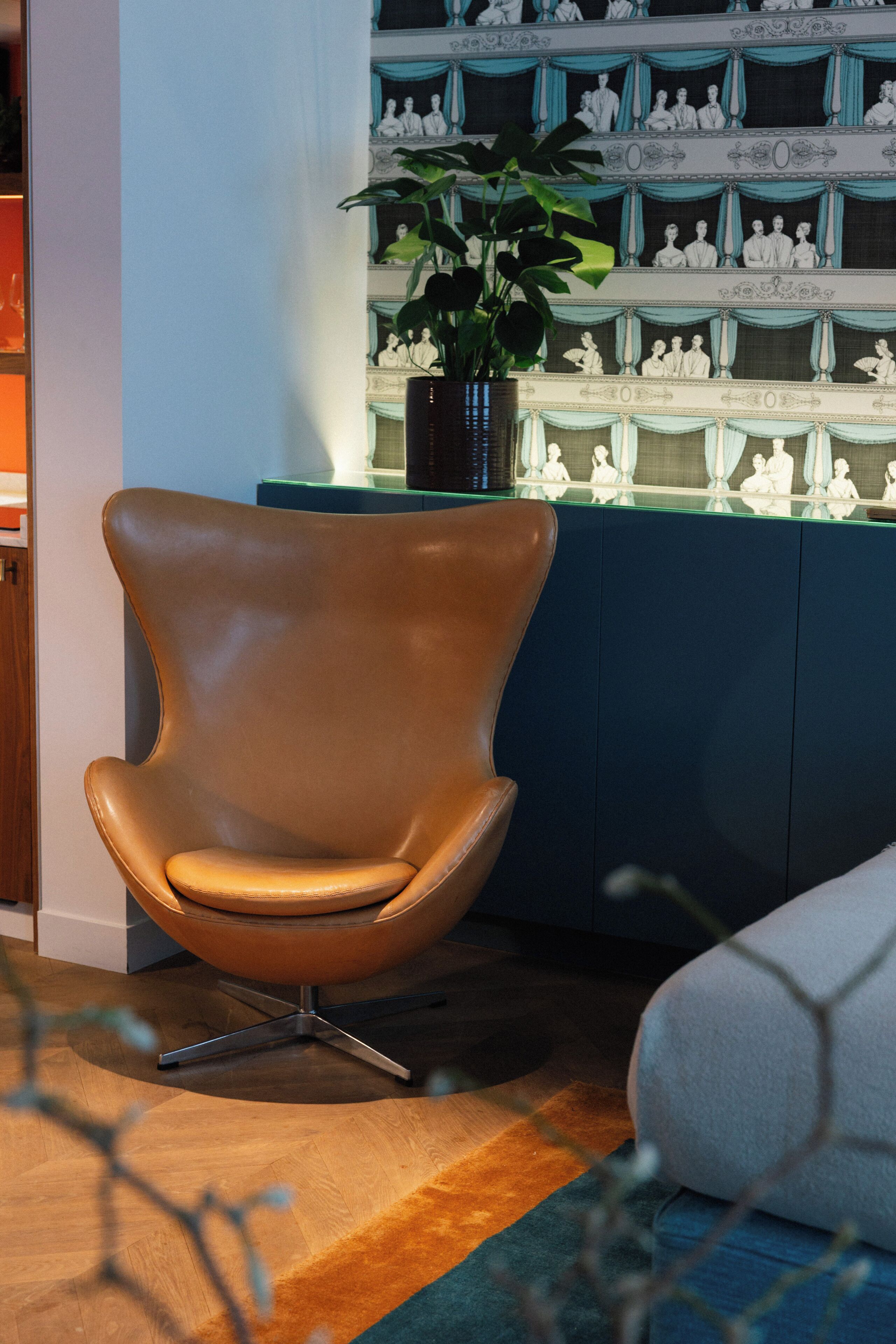 A modern interior with a brown leather chair, a blue cabinet with decorative items, and a plant.