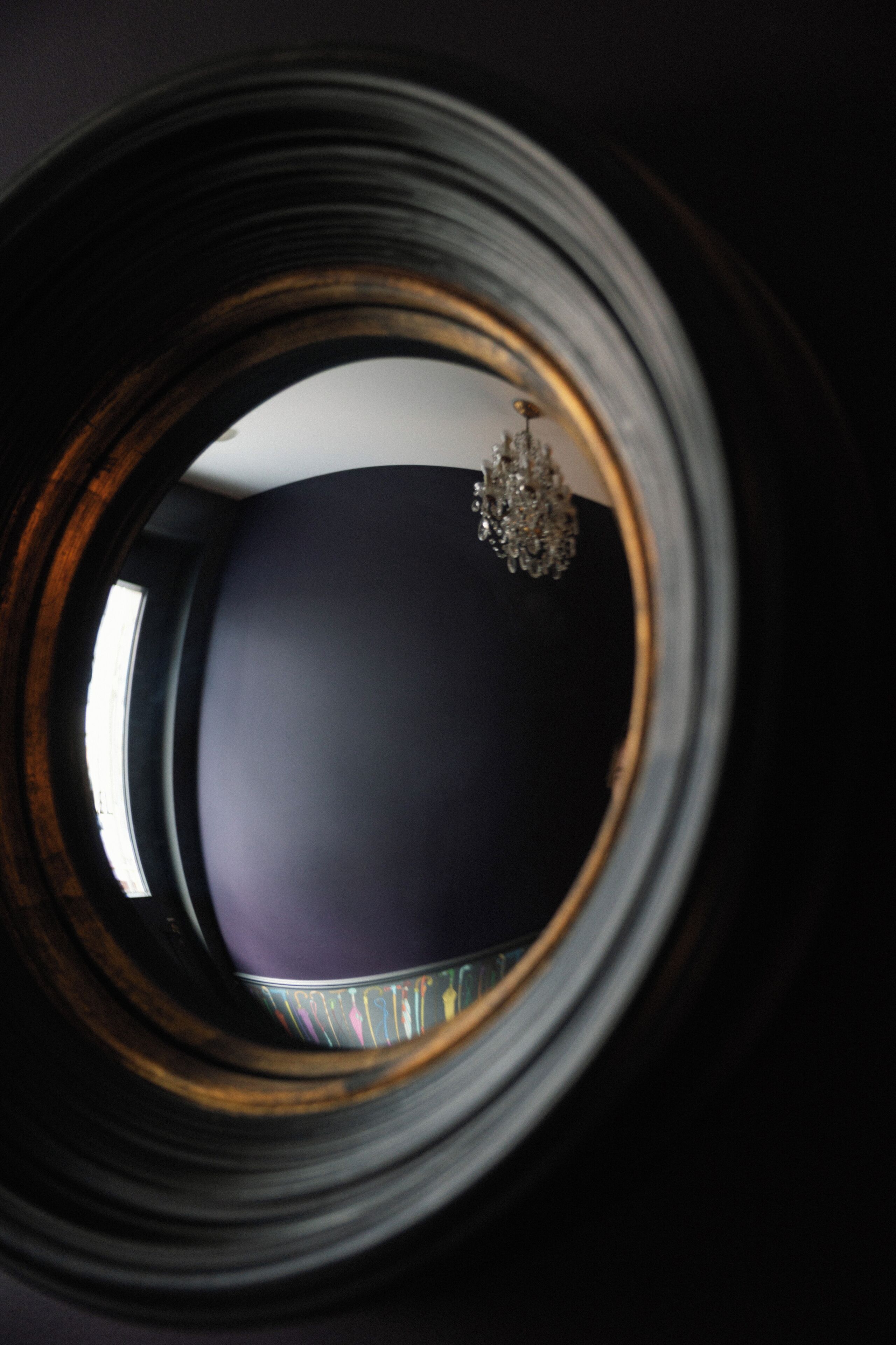 A view through a circular window with a chandelier visible in the reflection.