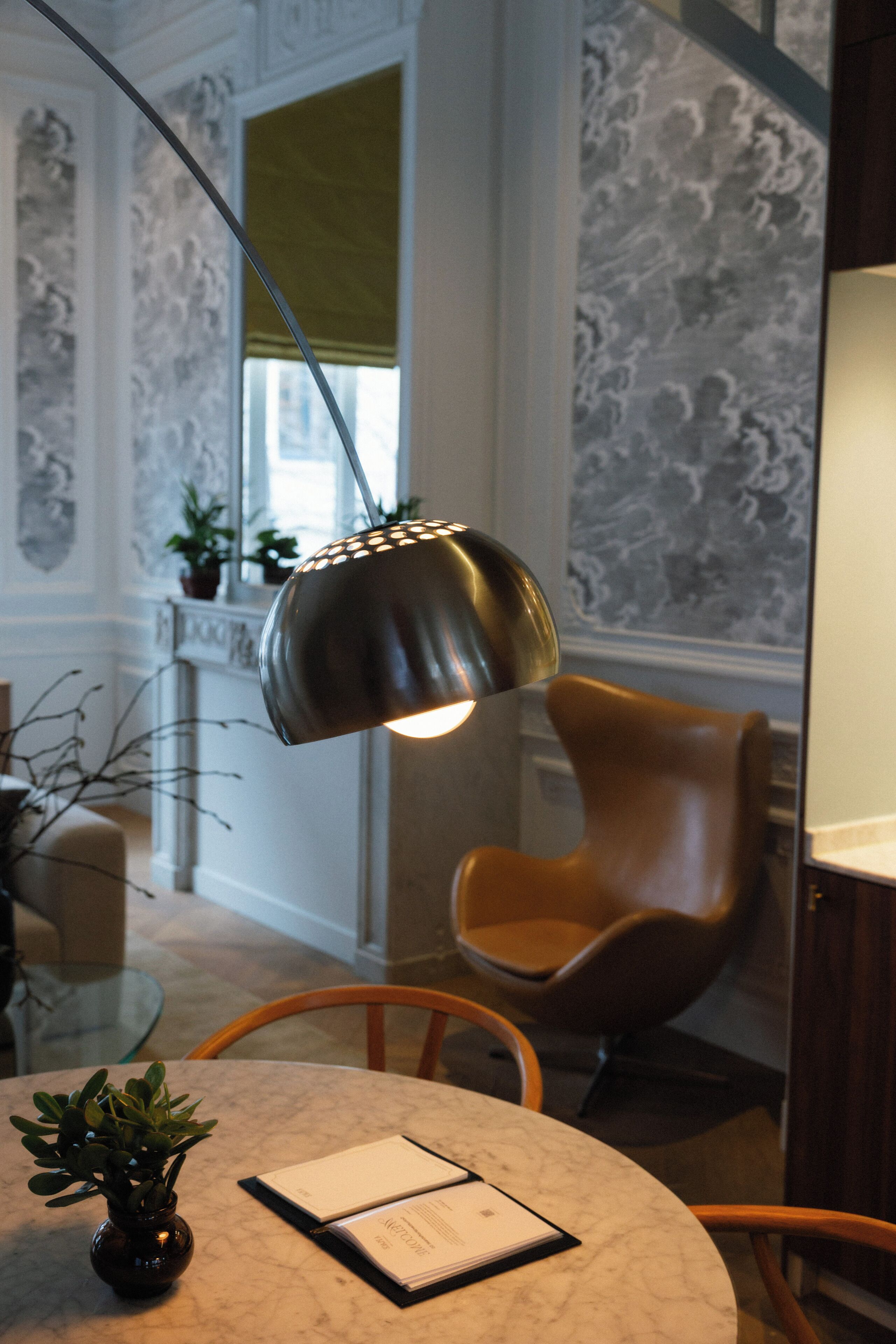 A round table with a vase and an open booklet, a modern chair, and a pendant light fixture.