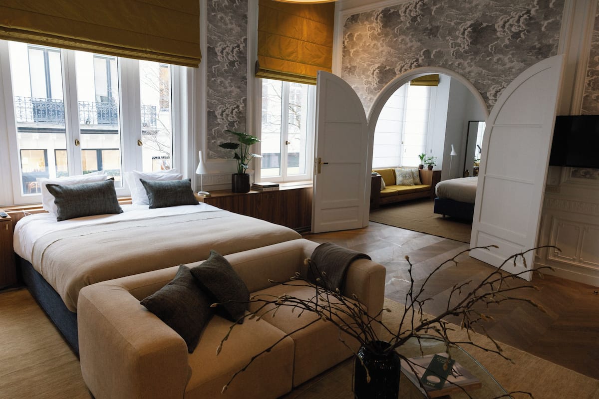 Une chambre moderne avec un grand lit, un canapé et une vue sur la ville grâce à de grandes fenêtres.