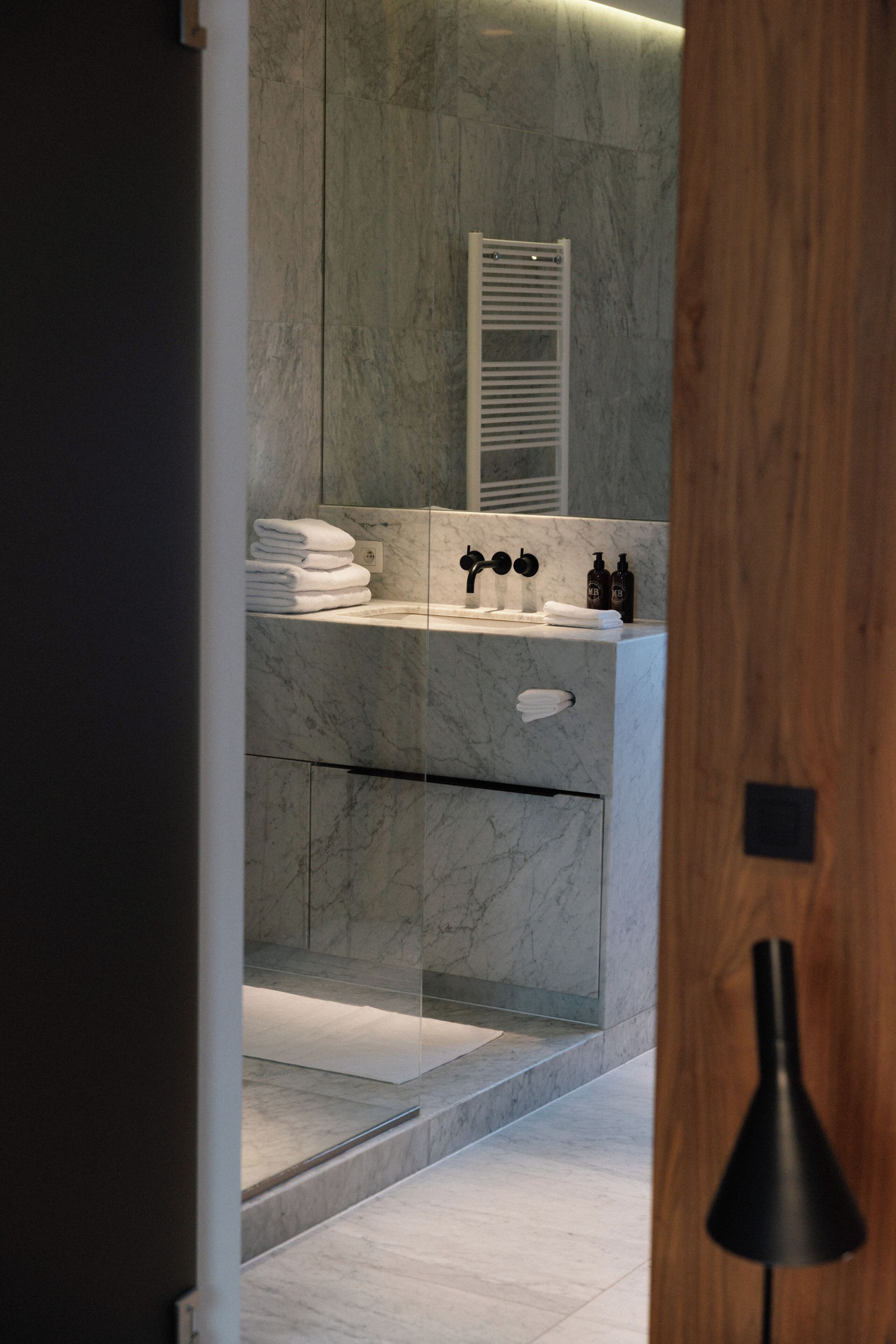 A modern bathroom with a marble sink, towel rack, and glass shower enclosure.