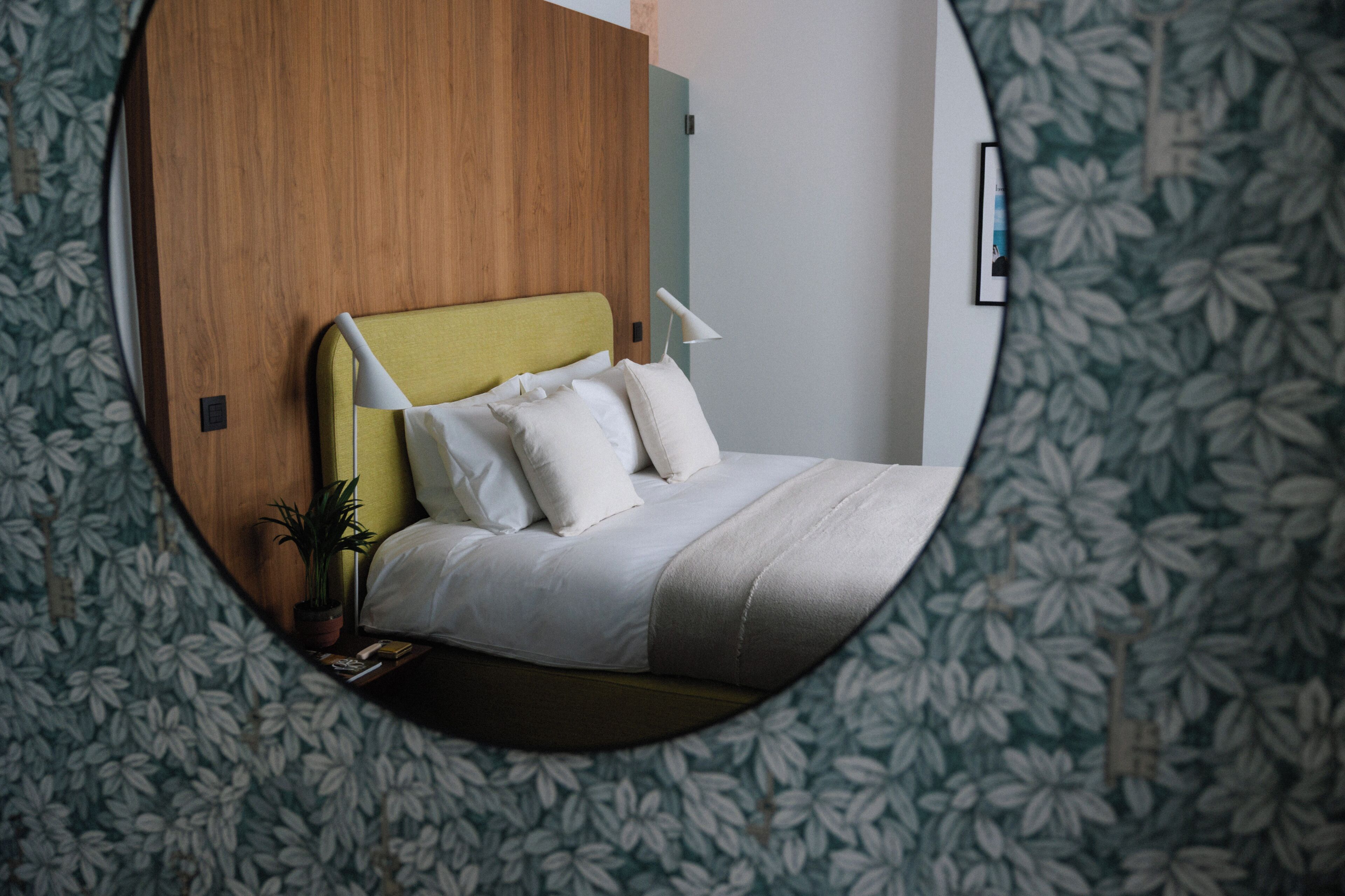 A circular view of a bedroom with a wooden headboard, a bedside lamp, and a bed with white bedding.
