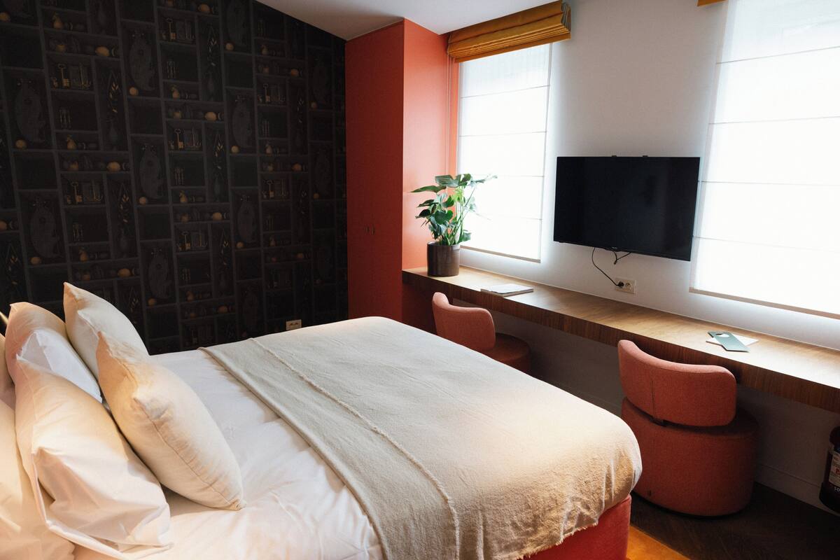 Une chambre d’hôtel avec un lit, un bureau équipé d’un ordinateur, une télévision et une fenêtre avec des stores.