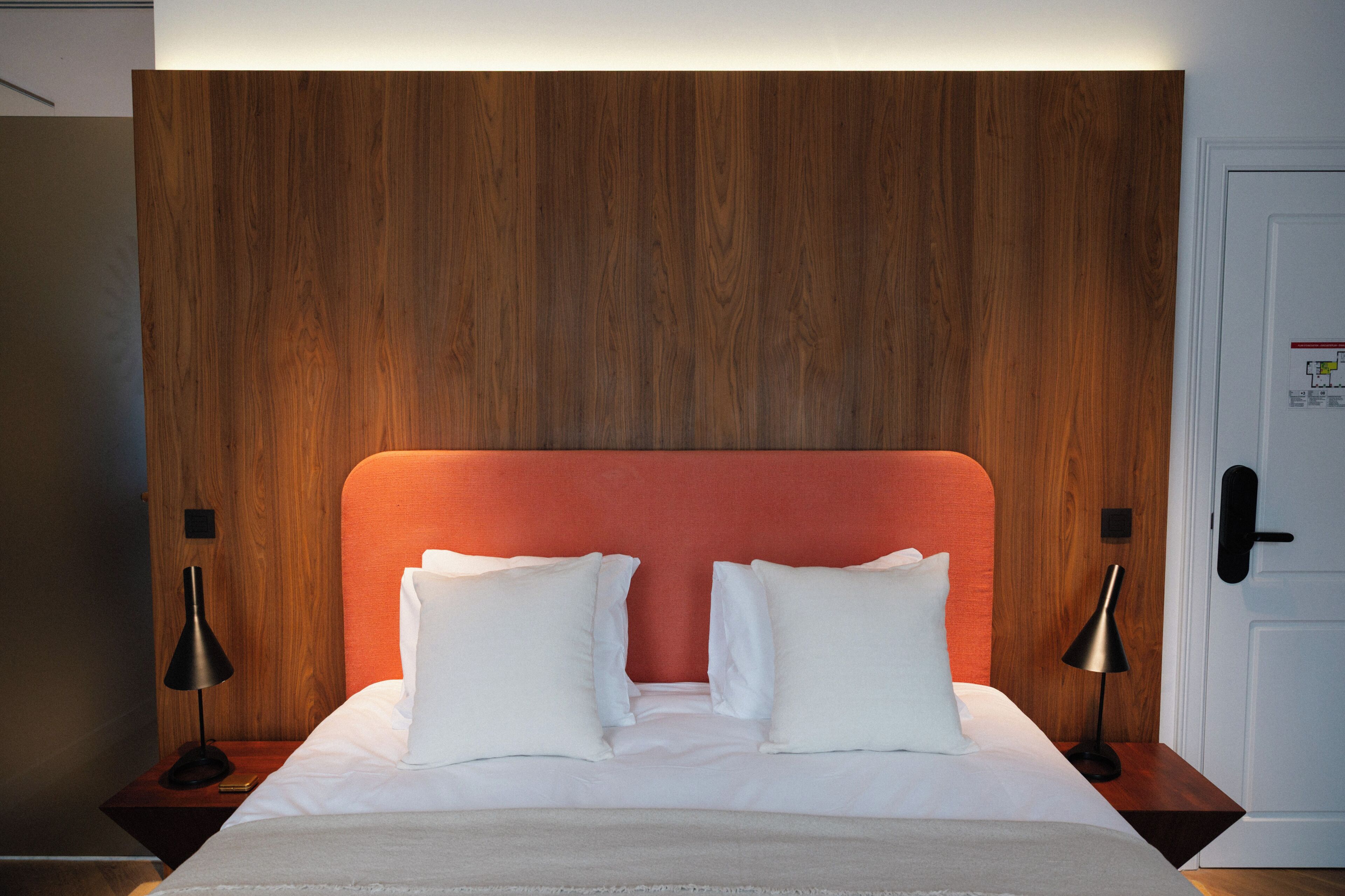 Una habitación de hotel con cabecera de madera, ropa de cama blanca y dos mesitas de noche con lámparas.