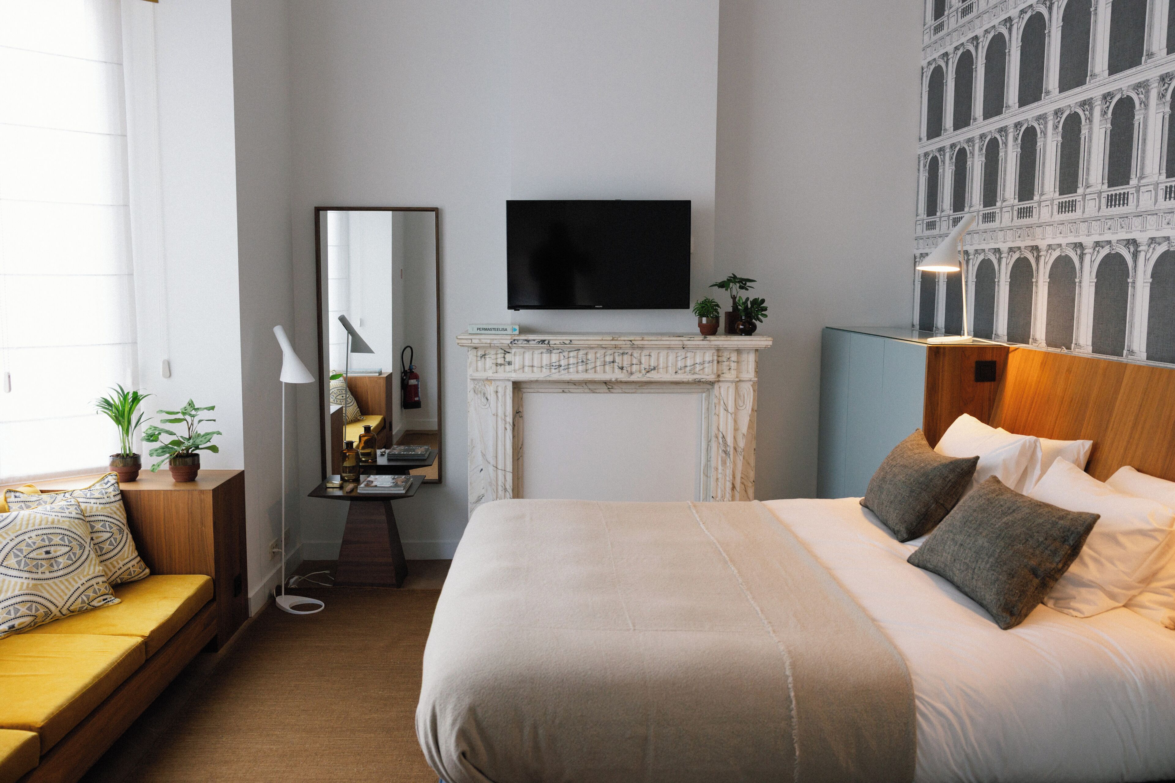 Una camera d'albergo con un letto grande, una TV a muro, un camino, un divano e uno specchio.