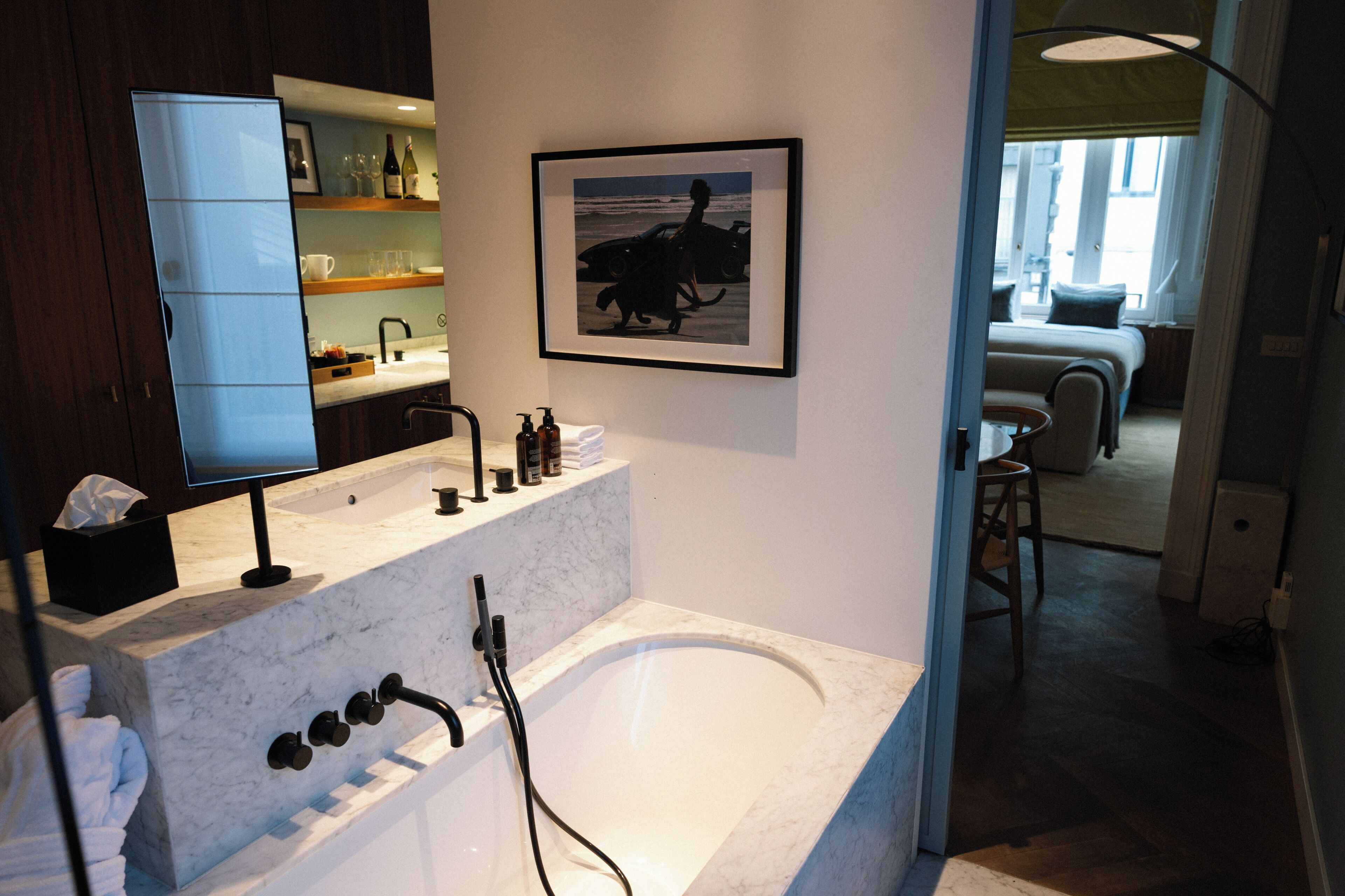 A modern bathroom with a marble sink, a large bathtub, and a framed picture of a woman with a dog on the wall.