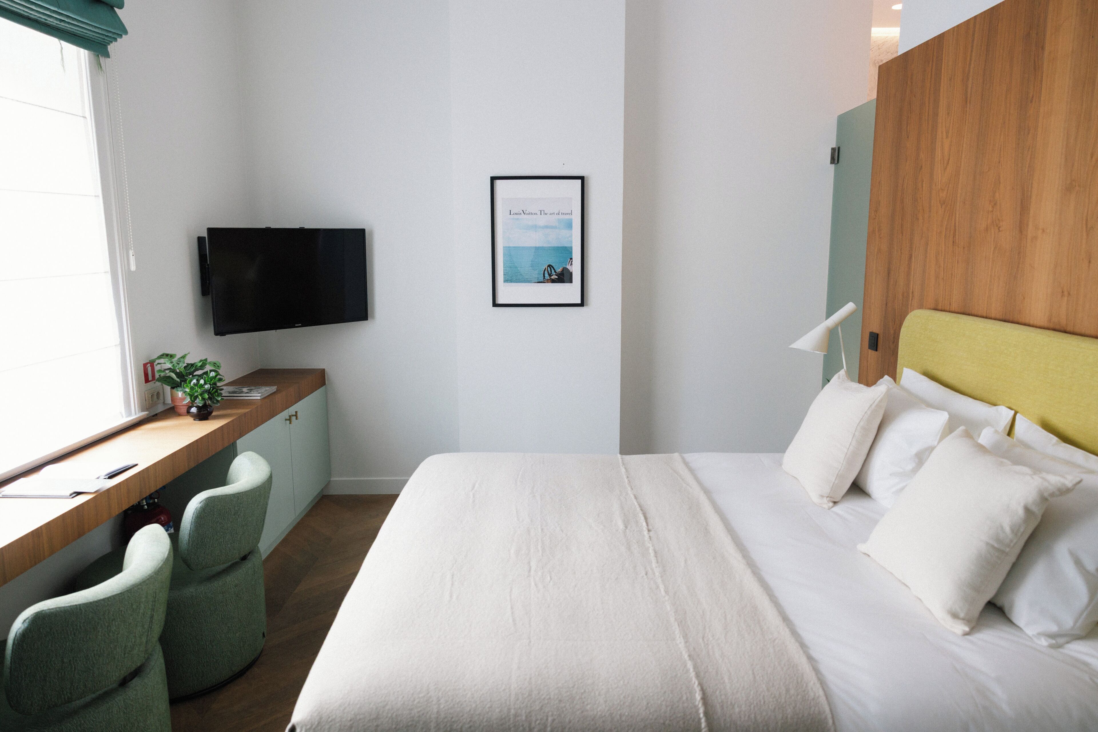 A hotel room with a bed, a desk with a chair, a television, and a framed picture on the wall.