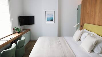 A hotel room with a bed, a desk with a chair, a television, and a framed picture on the wall.