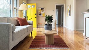 A living room with a grey sofa, a yellow door, a potted plant, and a wooden floor. - The Yellow Door Home for 8 (Franklin)