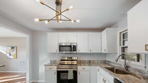 A modern kitchen with white cabinets, stainless steel appliances, and a marble countertop. - The Yellow Door Home for 8 (Franklin)