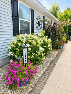 A residential building with a mailbox, a number sign, and a variety of flowering plants. - Walking distance to local eateries, watering holes, beaches, grocery & shopping! (Elk Rapids)