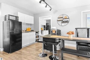 A modern kitchen with a black refrigerator, white cabinets, a wooden countertop, and a dining area with a black table and chairs. - Walking distance to local eateries, watering holes, beaches, grocery & shopping! (Elk Rapids)