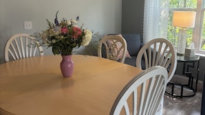 A dining area with a round table, white chairs, a vase of flowers, and a sign on the wall.
