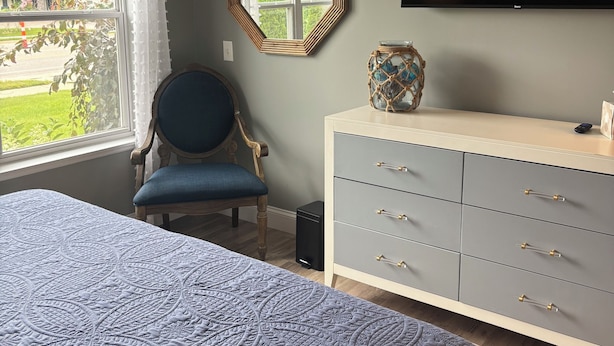 A bedroom with a bed, a chair, a dresser, a television, and a window with a view of greenery.