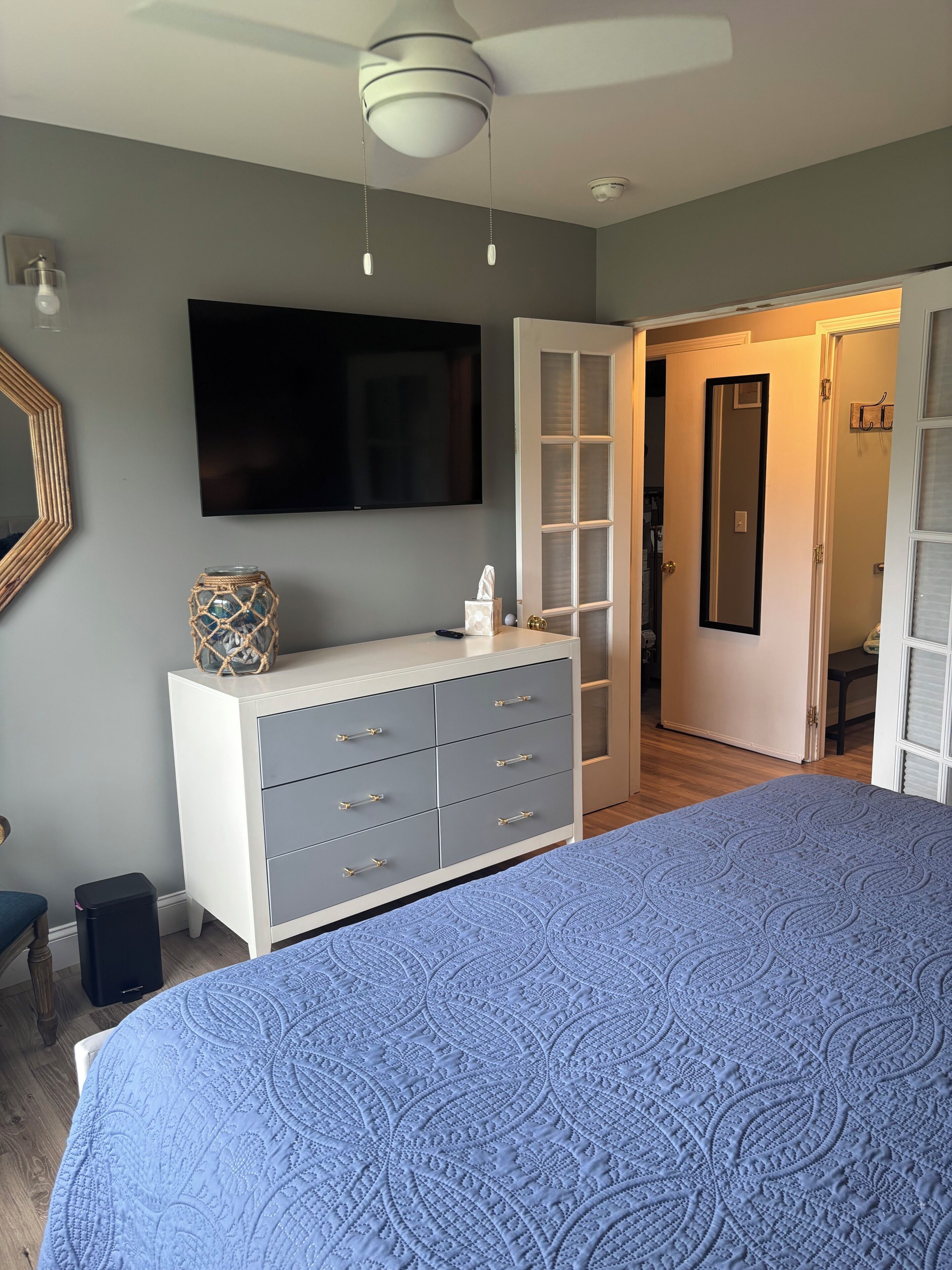 Une chambre à coucher comprenant un lit, une commode, une télévision et une porte donnant sur une salle de bain.