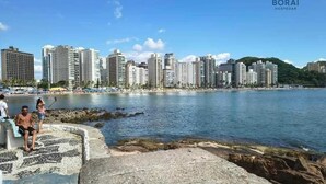 Un paisaje urbano costero con rascacielos, una costa rocosa y un cielo azul despejado.