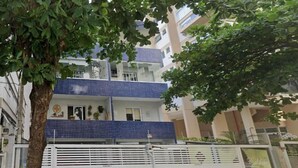 Un edificio residencial de varios pisos con fachada de azulejos azules, una entrada con reja y un árbol en primer plano.