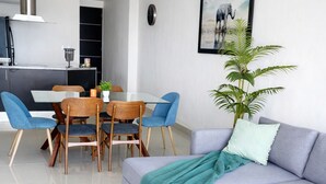 En moderne stue med en grå sofa, et spisebord med stole, et sofabord og en stor stueplante.