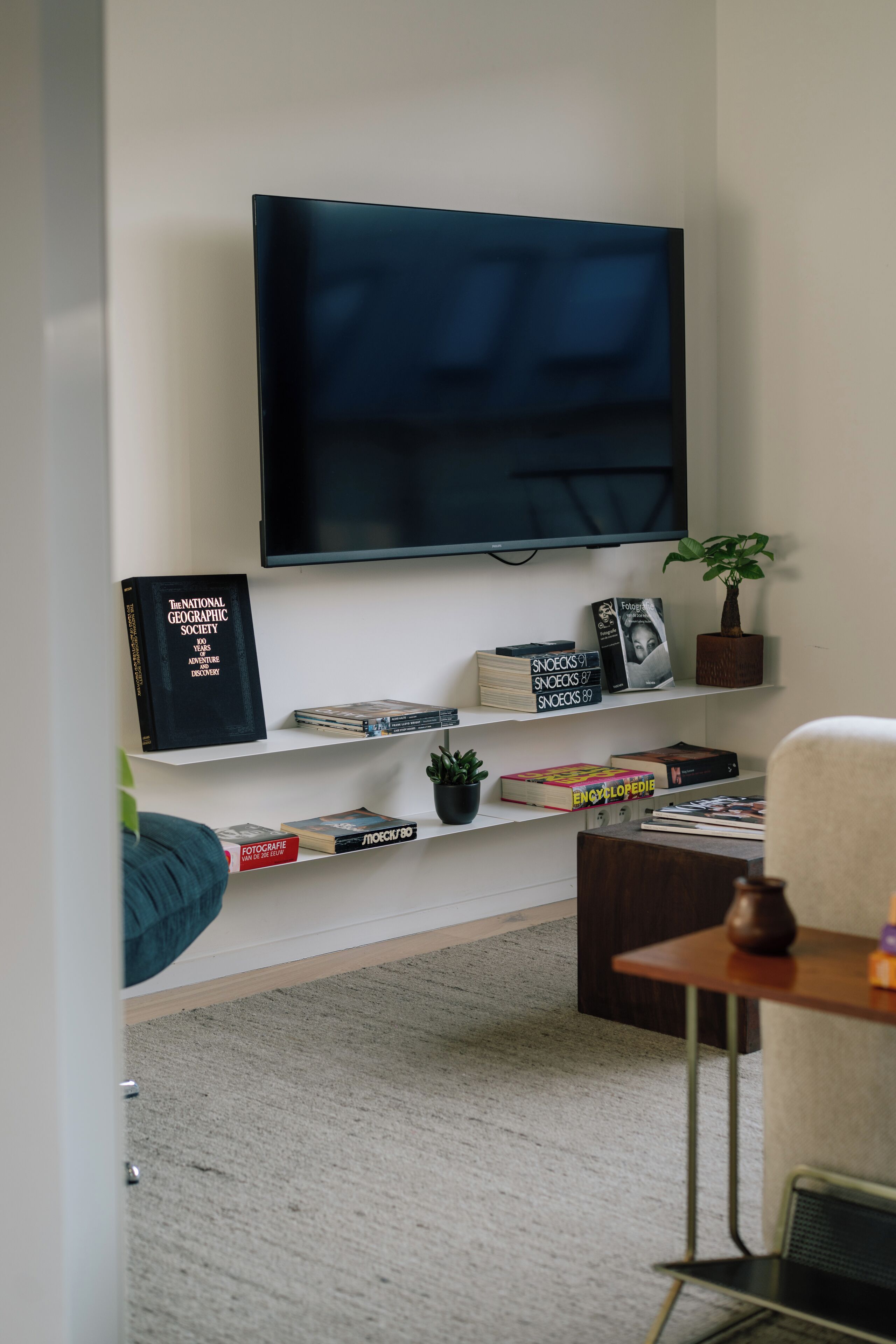 A living room with a flat-screen TV mounted on the wall, surrounded by bookshelves with various books and decorative items.
