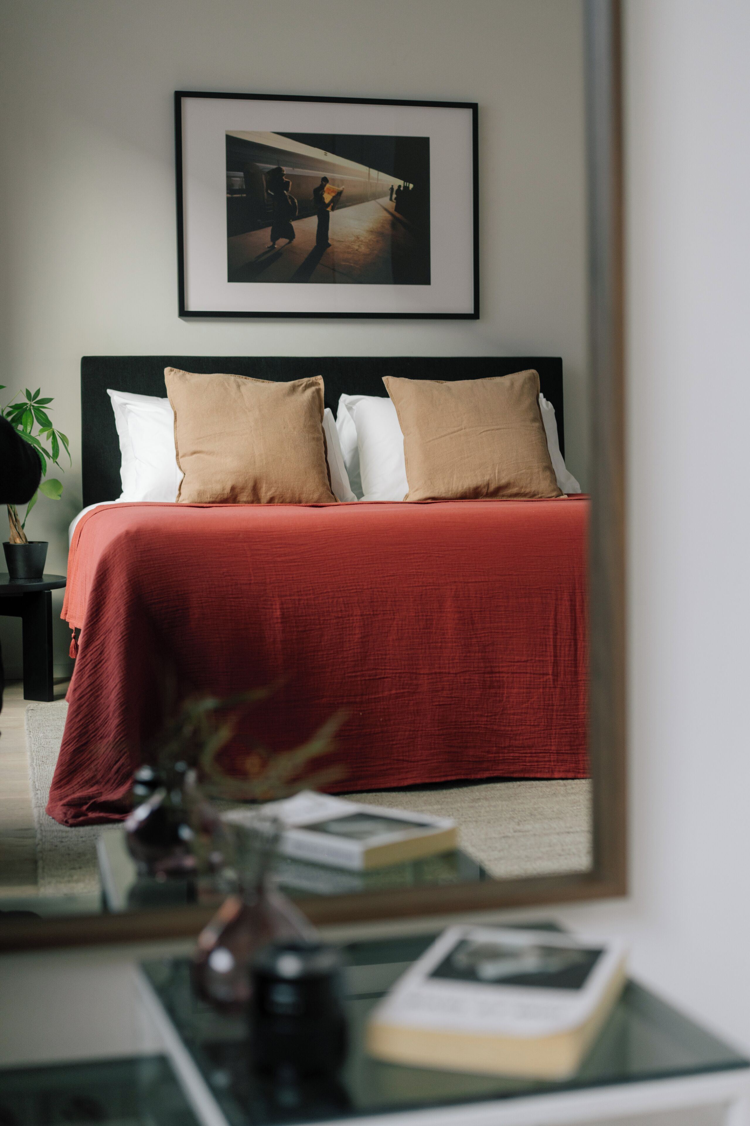 Een netjes opgemaakt slaapkamer met een groot bed, een ingelijst beeld erboven en een spiegel die de kamer weerkaatst.