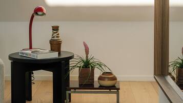 Ein Zimmer mit Holzboden, einem schwarzen Tisch mit roter Lampe, einer Vase und einem kleinen Regal mit Pflanzen.