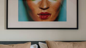 A framed artwork on a wall above a bed with beige pillows and a red bedspread.