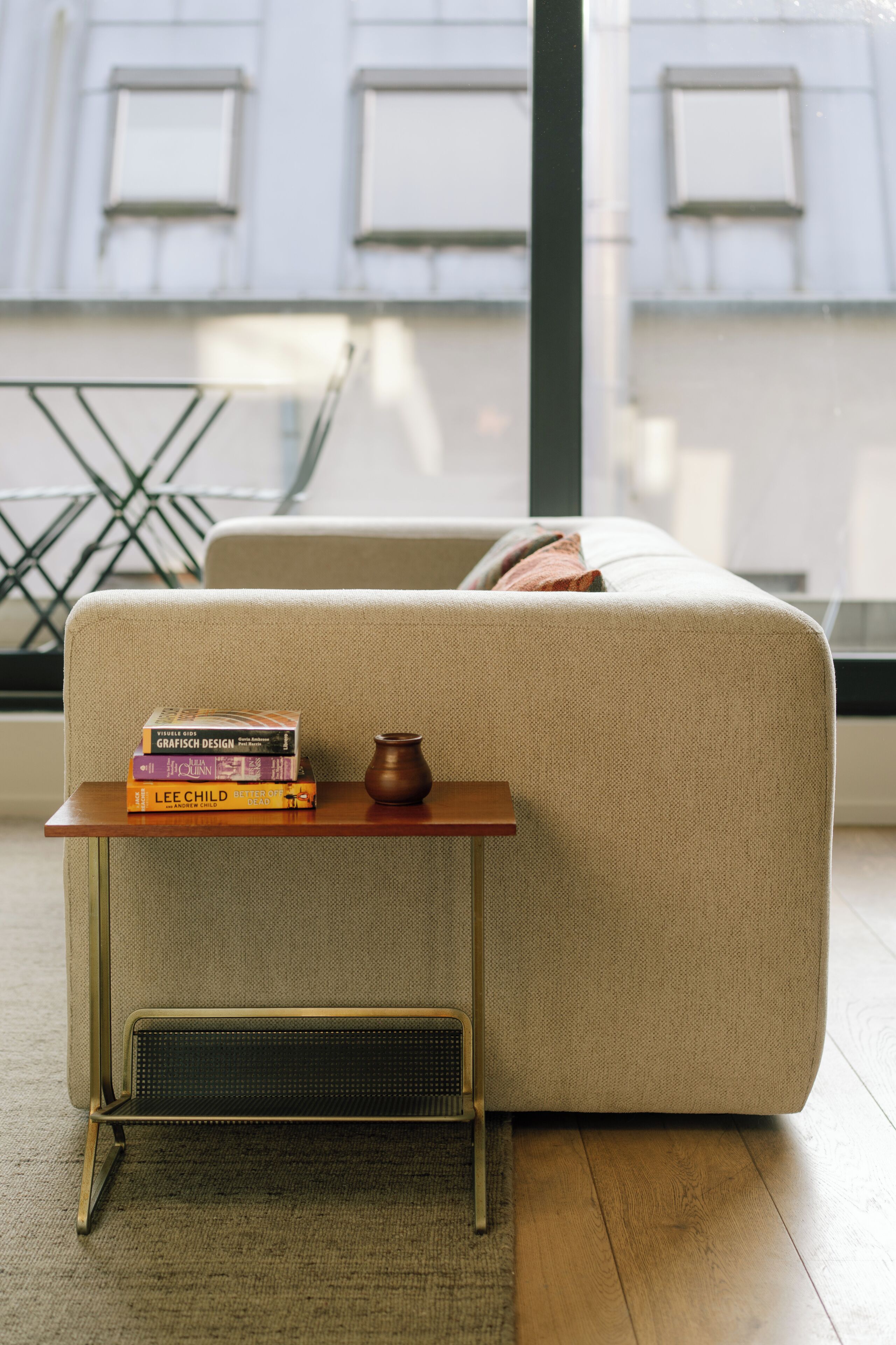 A modern living room with a sofa, a small wooden side table with books and a vase, and a radiator.