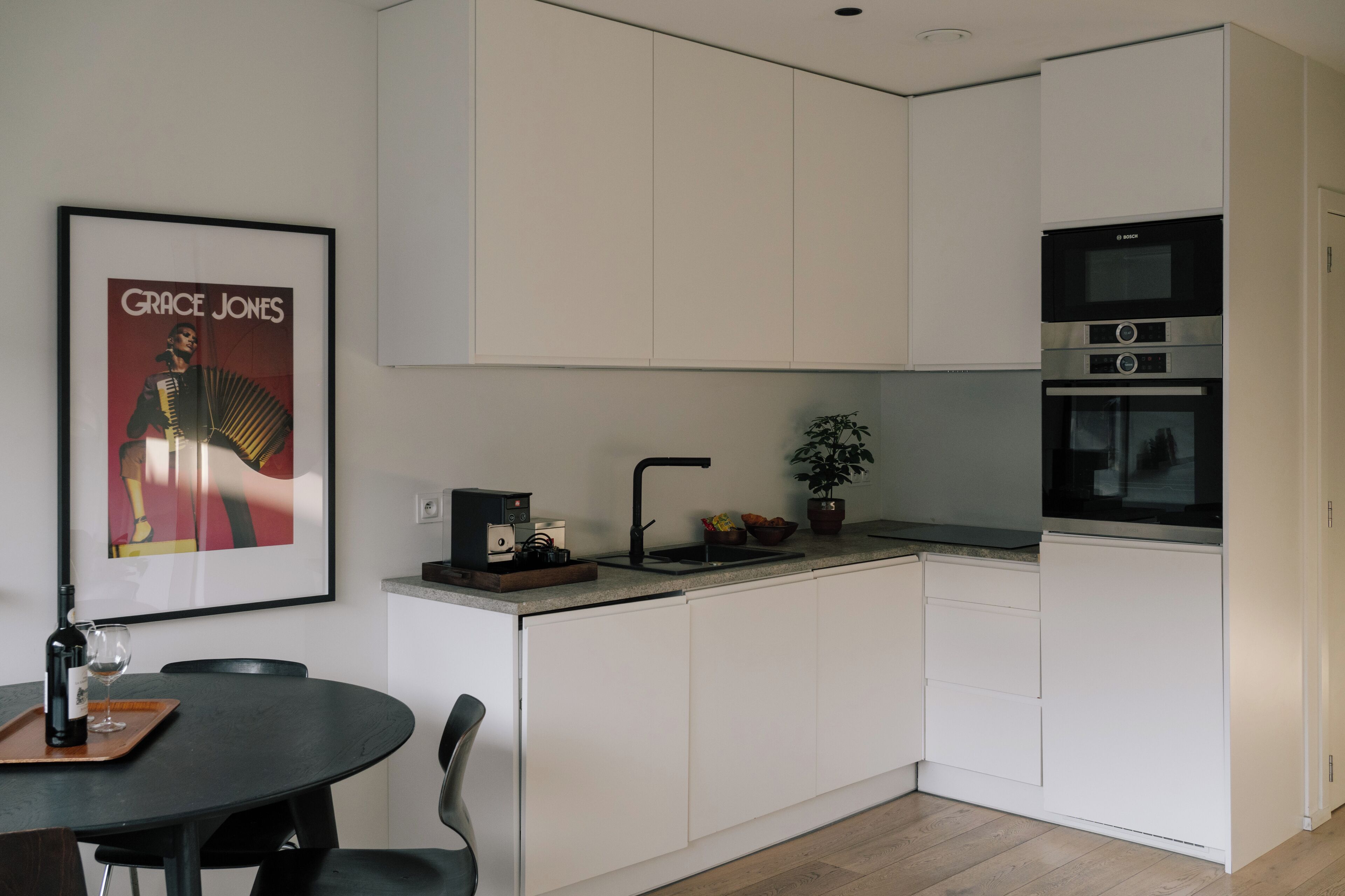 A modern kitchen with white cabinets, a Bosch oven, a sink, and a framed poster of Grace Jones.