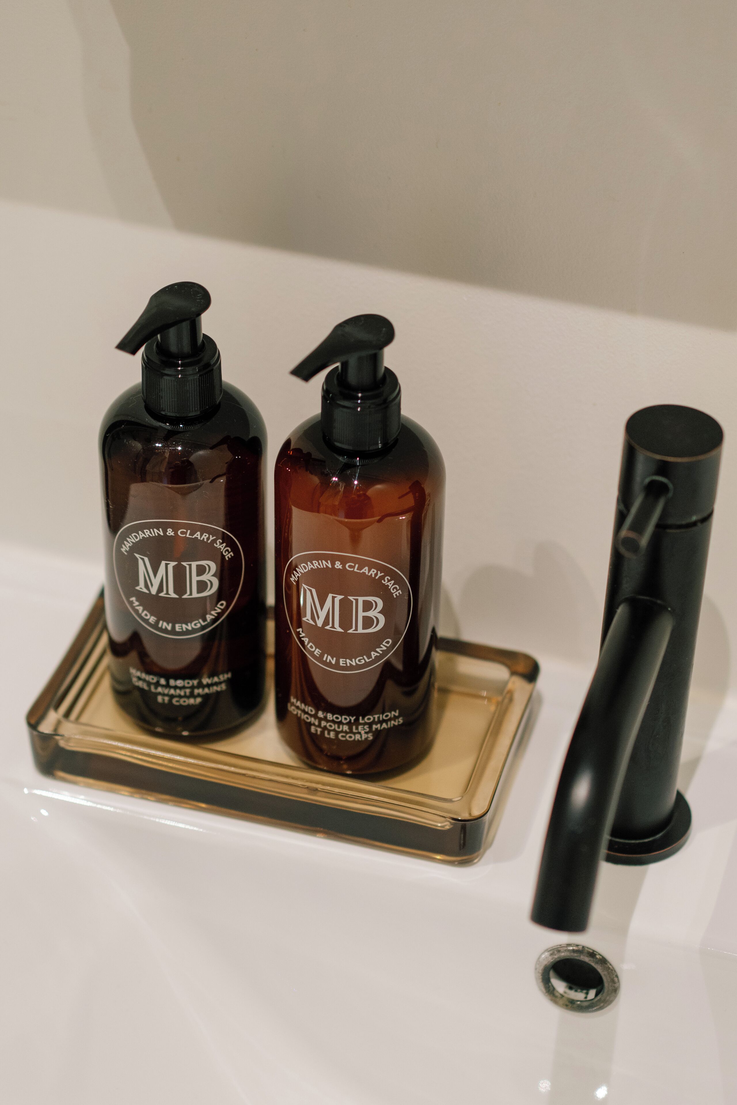 Two bottles of 'MB' body lotion on a tray with a black pump dispenser.