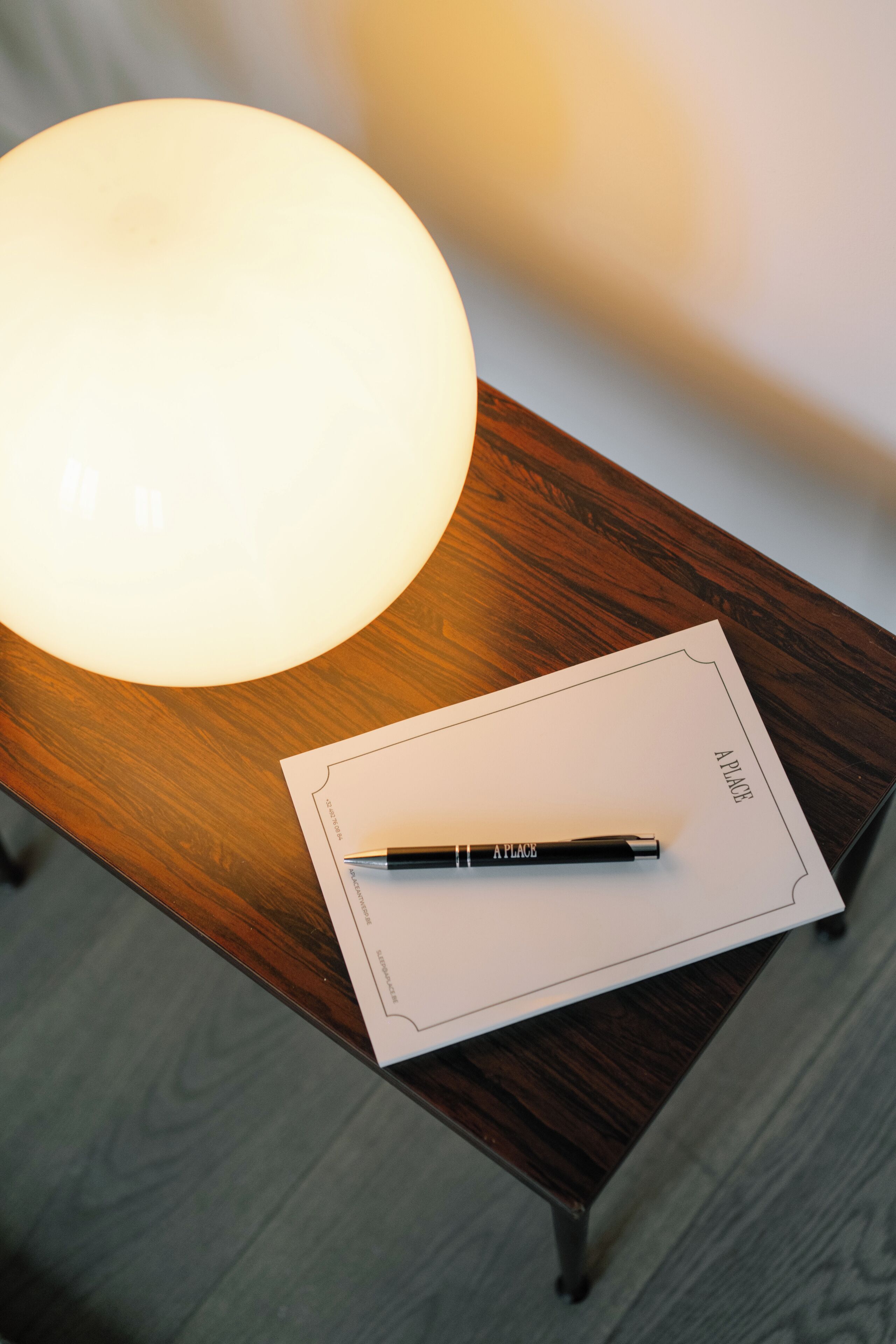 A wooden table with a white lamp, a pen, and a piece of paper with the word "PLACE" on it.