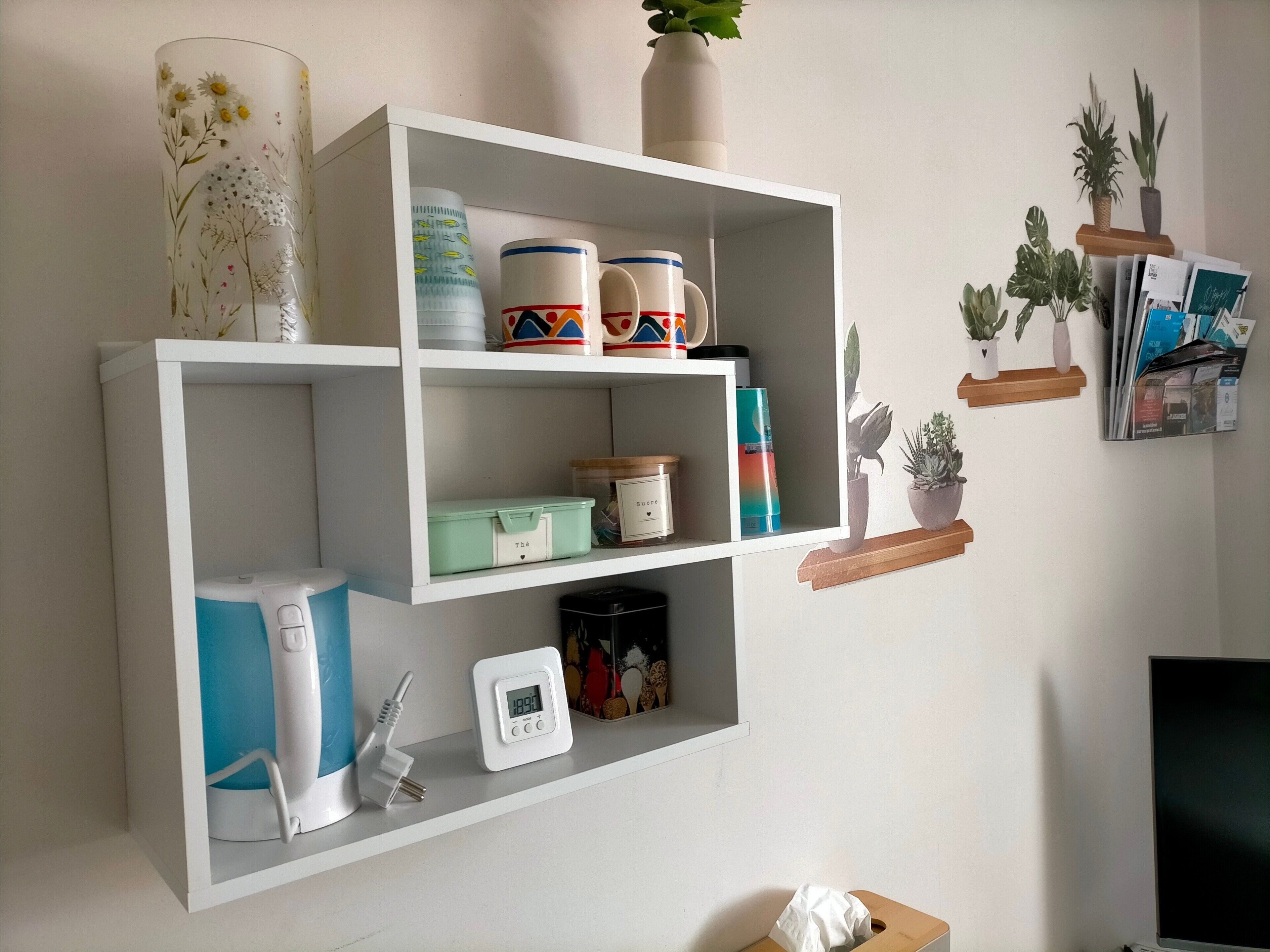 A white shelf unit with storage boxes, a coffee maker, a power strip, a digital clock, and decorative items.