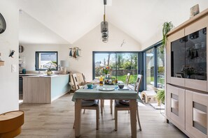 A modern kitchen with a dining area, large windows, and a view of the outdoors.