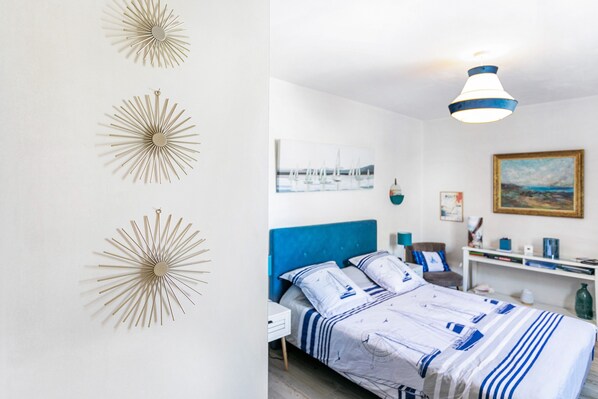 A bedroom with a bed, a nightstand, a chair, a desk, and wall art.