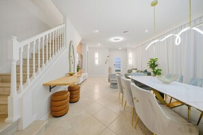 A spacious dining area with a long table, white chairs, and a staircase leading to another room. - 5BR house at Windsor Cay Resort (Clermont)