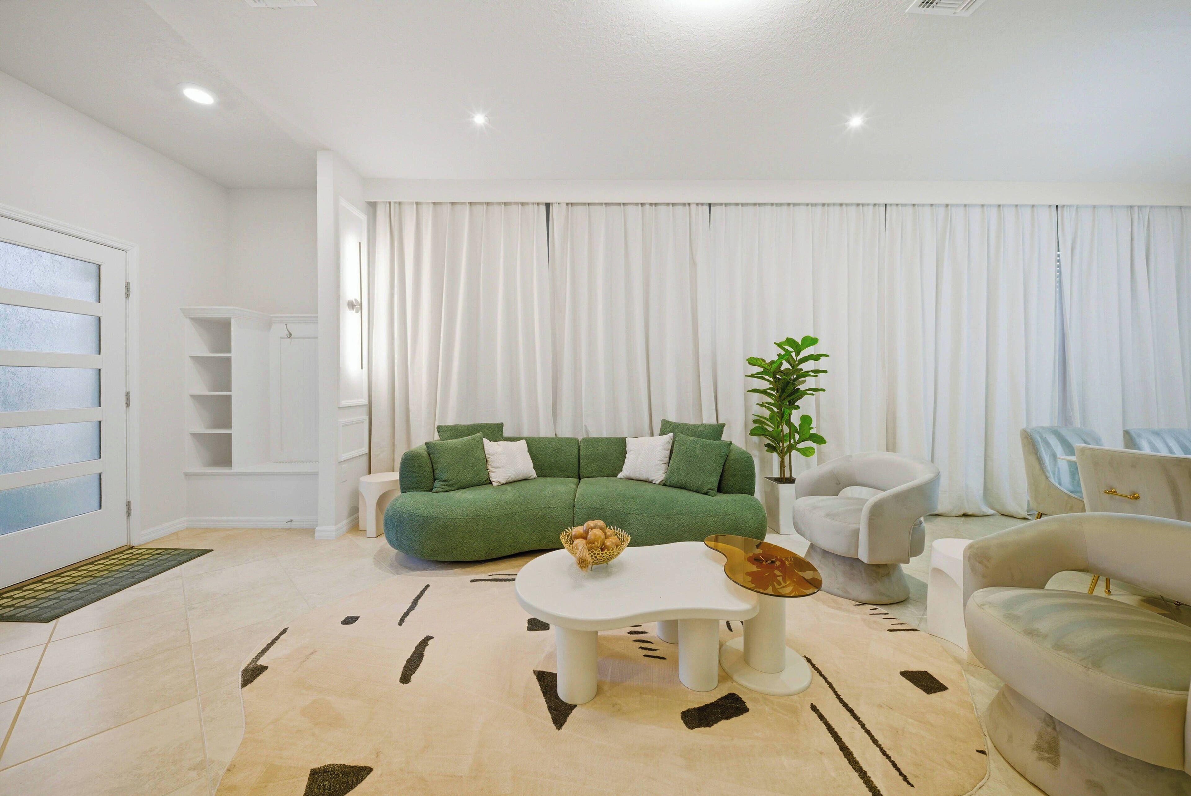A modern living room with a green sofa, white armchairs, a coffee table, and a potted plant.