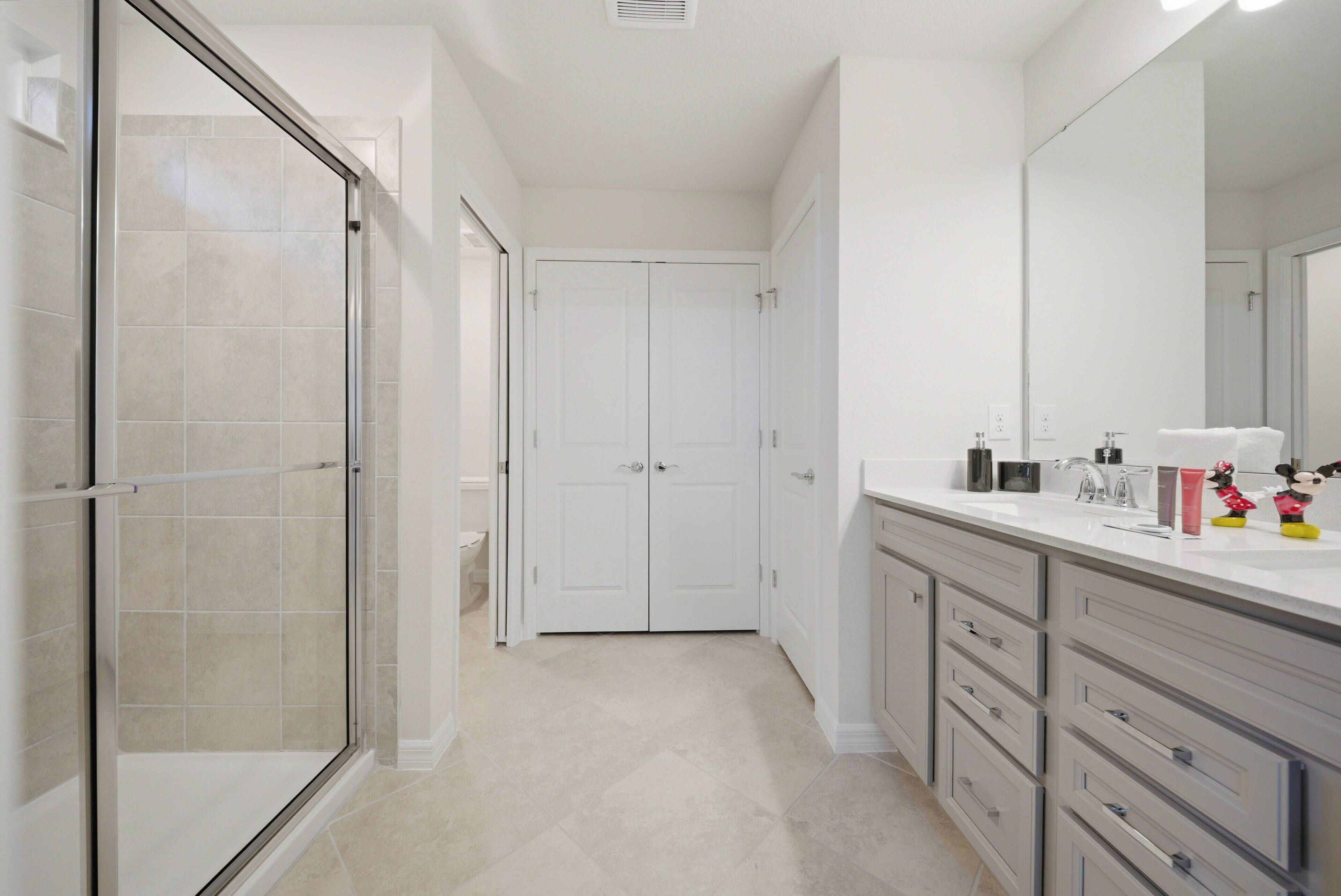 A modern bathroom with a glass shower enclosure, a walk-in closet, and a vanity with drawers and a mirror.