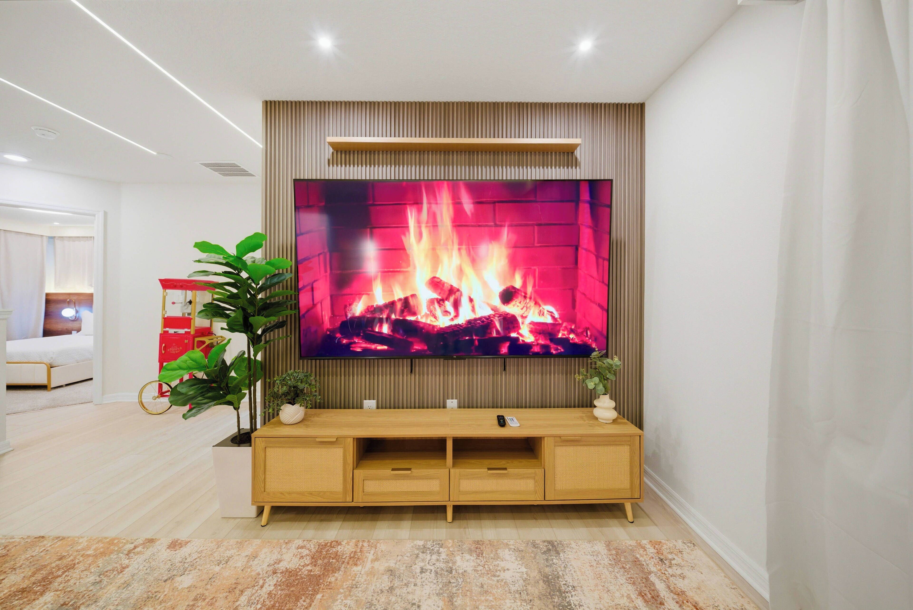 Un salon moderne avec un grand téléviseur à écran plat fixé sur une console en bois, une plante en pot et une petite voiture rouge jouet posée sur le sol.
