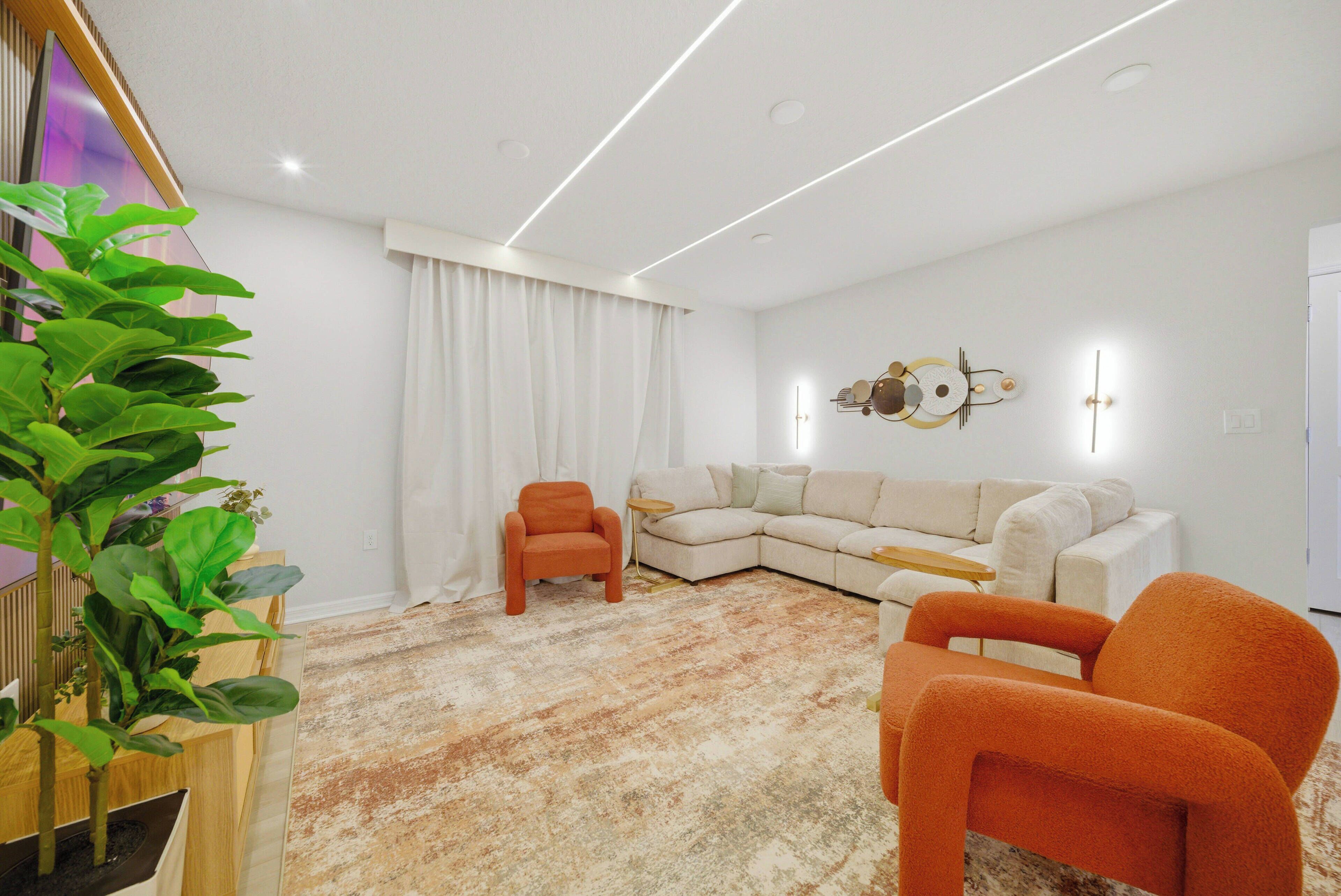 A modern living room with a sectional sofa, orange armchairs, a wooden plant stand, and a patterned carpet.