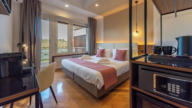 Ein Hotelzimmer mit Bett, Schreibtisch, Stuhl, einer Kaffeemaschine und Blick ins Freie.