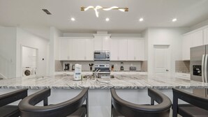A modern kitchen with white cabinets, a granite countertop, and a stainless steel refrigerator. - 9BR house sleeps 26 with spa in kissimmee (Kissimmee)