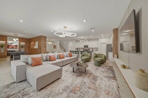 A modern living room with a sectional sofa, a coffee table, and a green armchair. - 9BR house sleeps 26 with spa in kissimmee (Kissimmee)