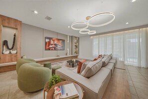 A modern living room with a sofa, green armchair, and a coffee table. There is a painting on the wall and a pendant light fixture above the seating area. - 9BR house sleeps 26 with spa in kissimmee (Kissimmee)