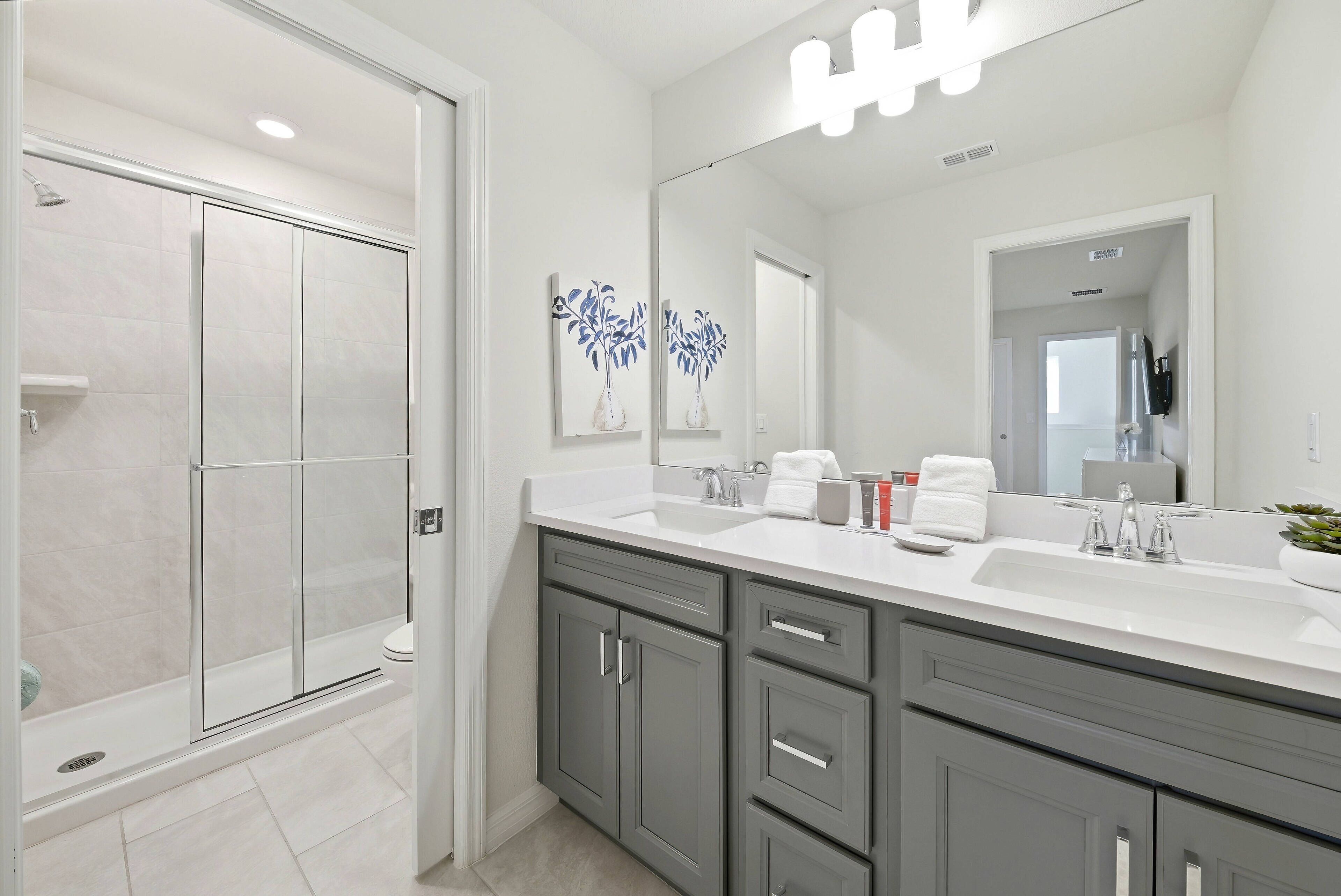 Un baño moderno con cabina de ducha, un espejo grande y un mueble de tocador doble.