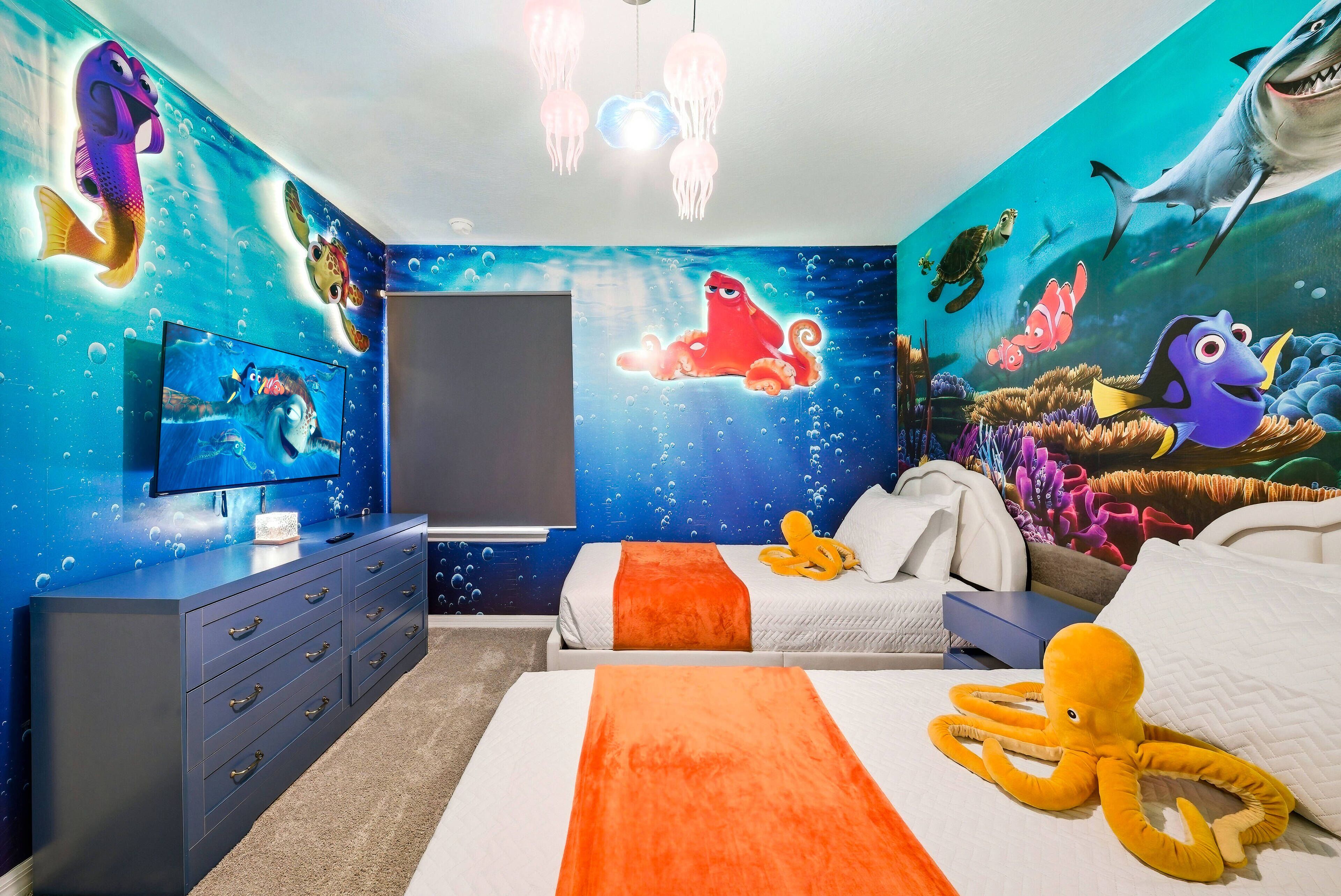 A bedroom with a mural of ocean creatures, a bed with an orange blanket, and a TV on a dresser.