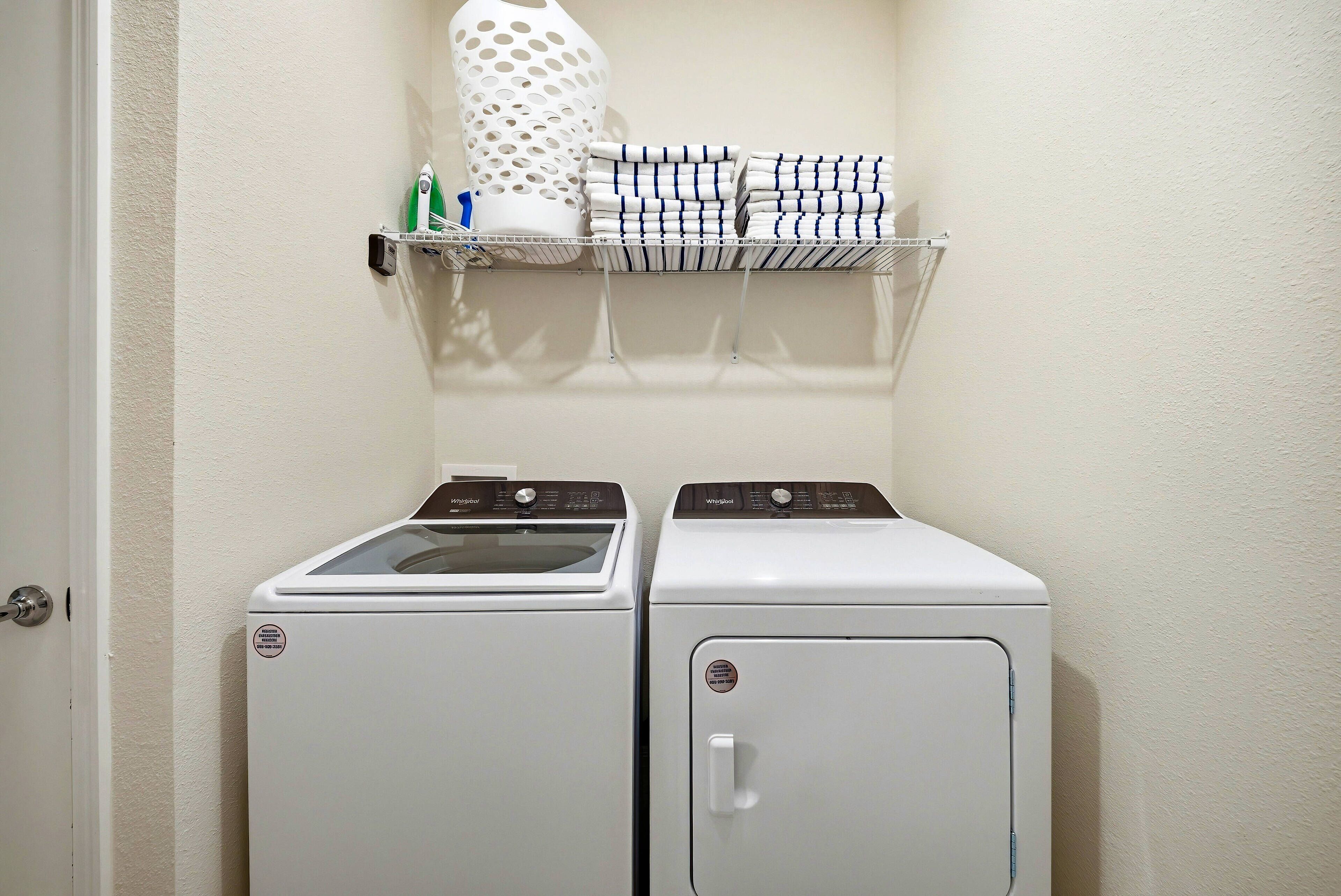A laundry area with two white front-loading washers and dryers, a shelf with folded towels, and a white vase.