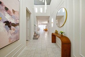 A hallway with a large abstract painting, a wooden console table with a mirror, and a staircase leading to another room. - 8BR house at Windsor Cay Resort (Clermont)