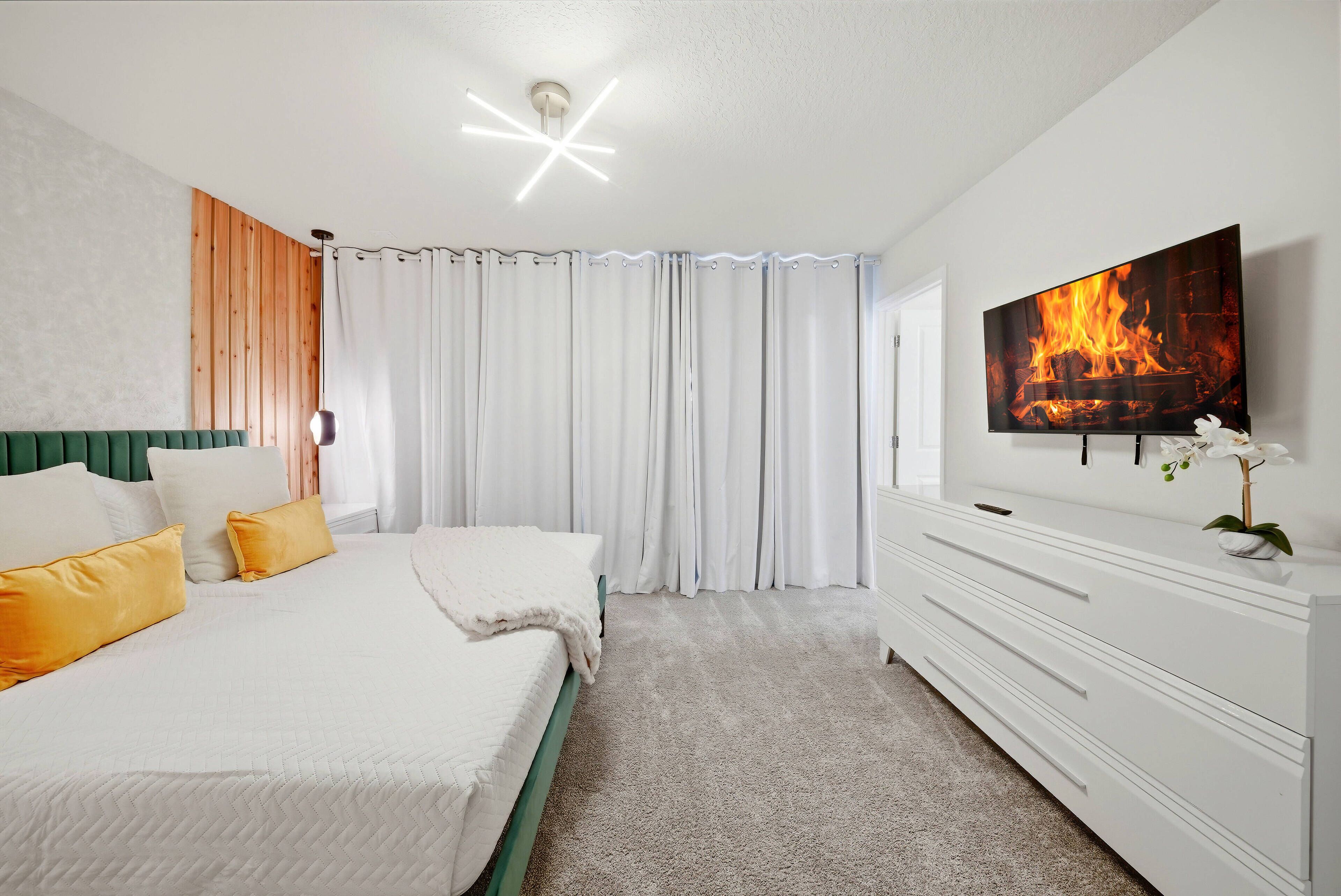 Une chambre à coucher avec un lit, une télévision, une commode et un rideau.