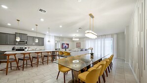 Een moderne keuken met grijze kastjes, een centraal eiland, en een eethoek met gele stoelen en een glazen tafel.